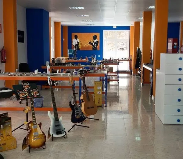 Bancos de trabajo del taller, con guitarras y bajos delante y un mural de músicos al fondo